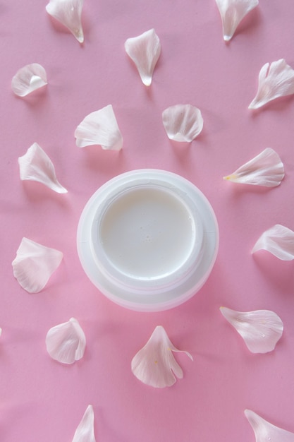 Organic skin care product and delicate flower petals on pink background. Healthy cosmetic products . Wellness beauty treatment.