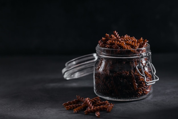 Organic uncooked Buckwheat Fusilli pasta in a glass jar on a dark background. Wholegrain gluten free noodles. Healthy food concept.