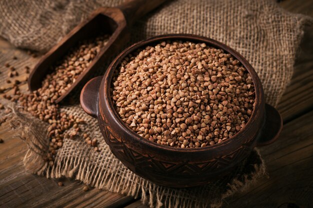 Organic uncooked scattered buckwheat grain in a bowl and wooden scoop on a rustic wooden background. Healthy and diet food concept.