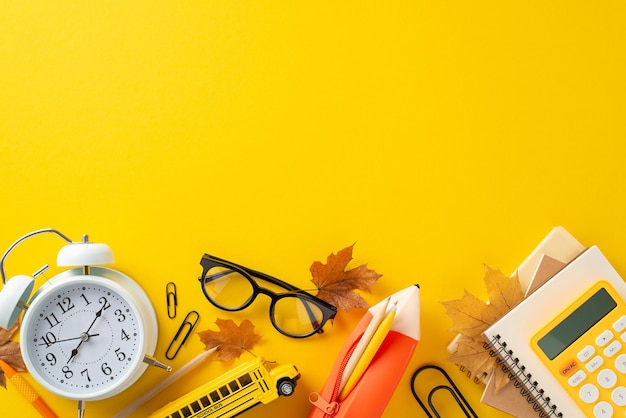 Organize your study space top view various school supplies like copybooks pencil case calculator clock and more Vibrant yellow background decorated with maple leaves perfect for promo message