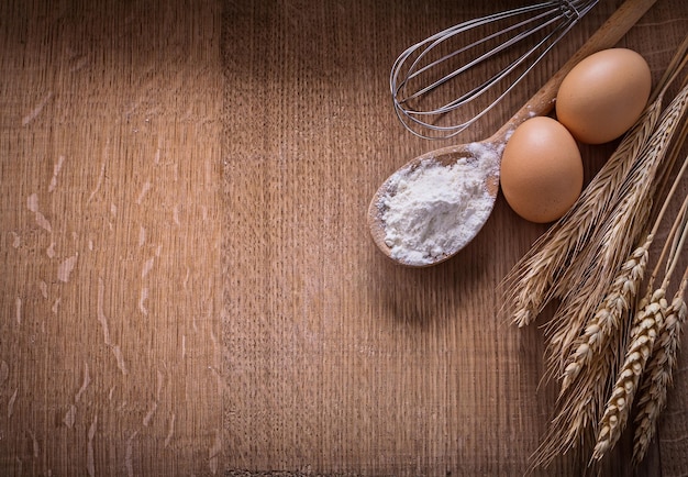 Organized copyspace flouur in spoon eggs ears of wheat corolla on wooden board food and drink still life