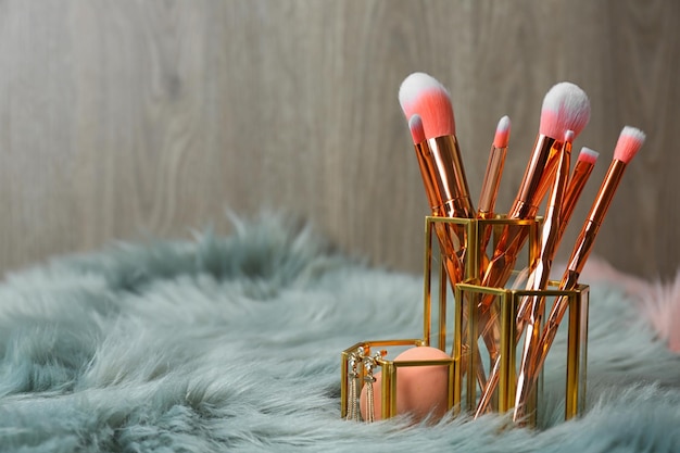 Organizer with set of professional makeup brushes and accessories on furry fabric against wooden background Space for text