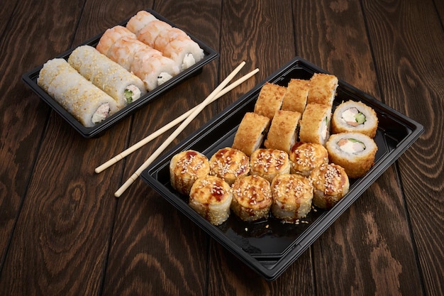 Oriental cuisine rolls in plastic takeout trays on a wooden table close up