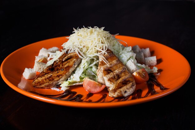 Oriental salad with chicken on an orange plate, beautiful serving, dark surface.