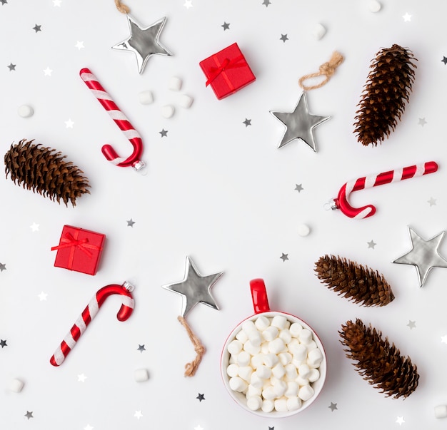 Ornaments, pine cones, cup of hot chocolate with marshmallow and red gift boxes on a white background