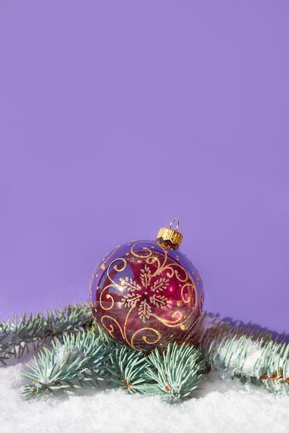 Ornate glass bauble ball on fir twigs under snowPurple paper background with copyspace Traditional Xmas arrangement Merry Christmas and Happy New Year