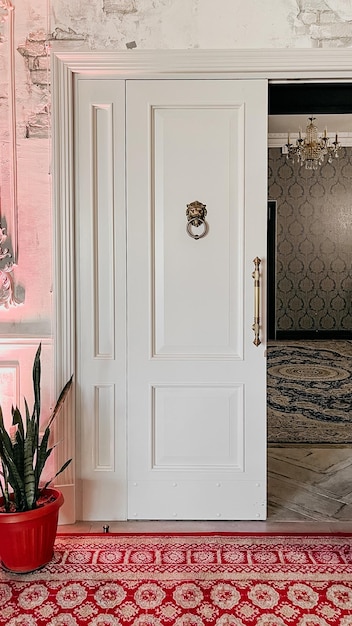 Ornate gold door knocker on white door with red patterned rug