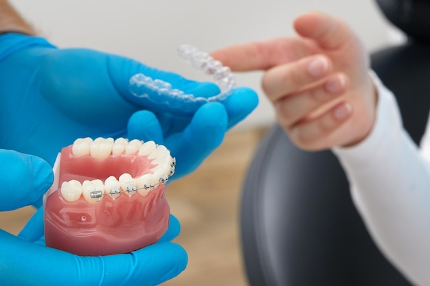 Orthodontist showing model of human jaw with wire braces and aligners explaining the difference