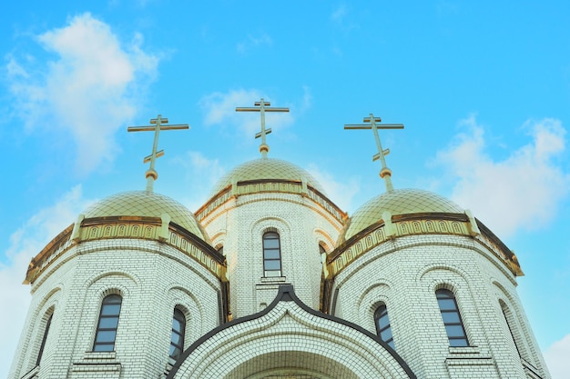 Orthodox brick church with golden domes and 3 crosses against the backdrop of a beautiful cloudy sky.