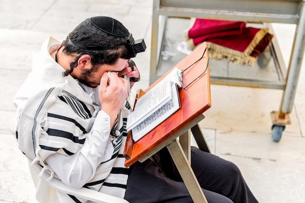 Photo orthodox jewish man with phylacteries tefilin and shawl tallit covering his eyes with the tzitziot of the shawl during prayer