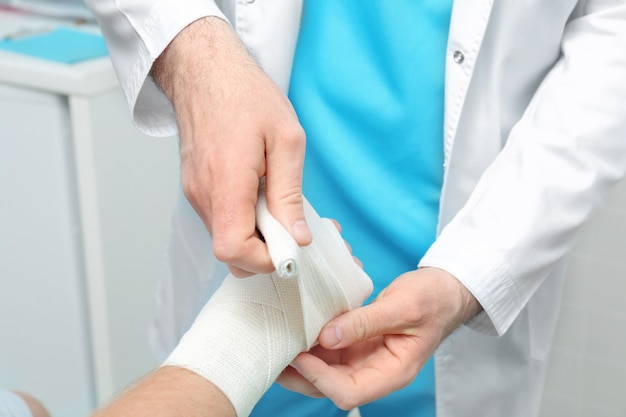 Orthopedist applying bandage onto patient's hand in clinic, closeup