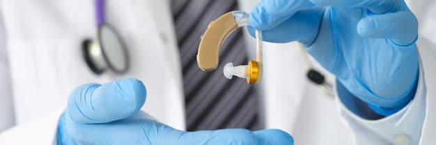 Otorhinolaryngologist holding hearing aid with rubber gloves closeup