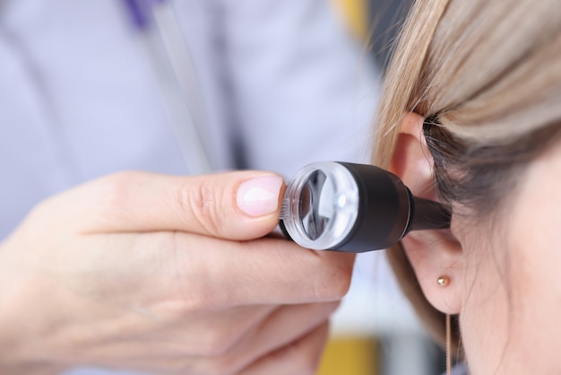 Otorhinolaryngologist looking at patients ear using an otoscope closeup.