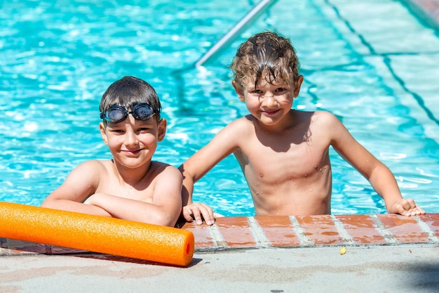 Oudoor summer activity Concept of fun health and vacation A happy brothers boys eight and five years old in swimming goggles are holding onto the side of the pool on a hot summer day