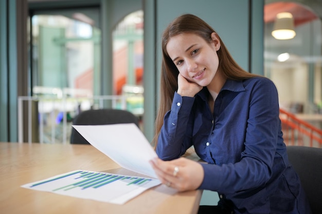 Oung concentrated businesswoman holding pen filling document or tax form making notes on paper