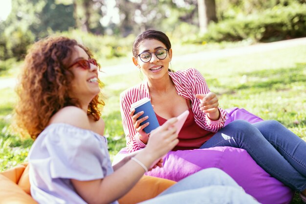 Our day together. Exuberant dark-haired woman drinking coffee and relaxing with her friend in the open air