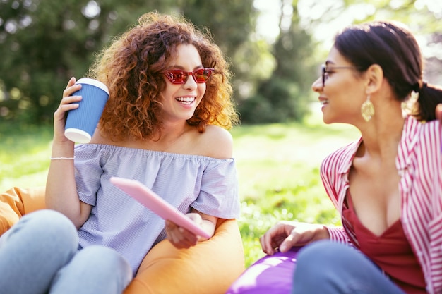 Our recreation. Pretty inspired woman holding a tablet and talking with her friend