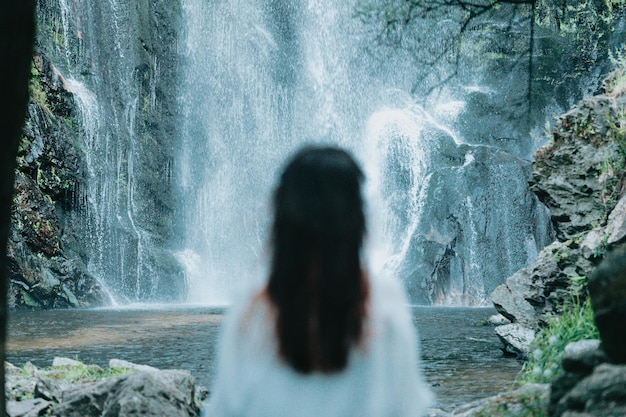 Out of focus young woman resting and looking a waterfall meditation yoga and thinking concepts freedom in nature independent lifestyle and freedom concept Natural parade and pure air concept