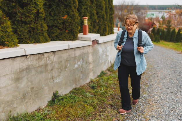 Outddor portrait of happy European female pensioner with backpack enjoying beautiful nature while nordic walking Aging people active lifestyle and health concept