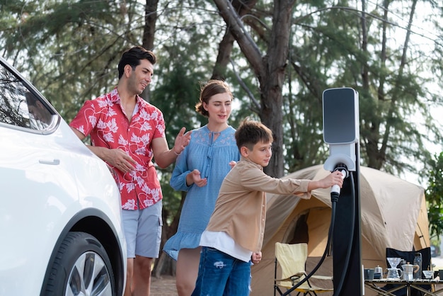 Outdoor adventure and family vacation camping in nature travel by eco friendly car for sustainable future Lovely family recharge EV car with EV charging station in campsite Perpetual