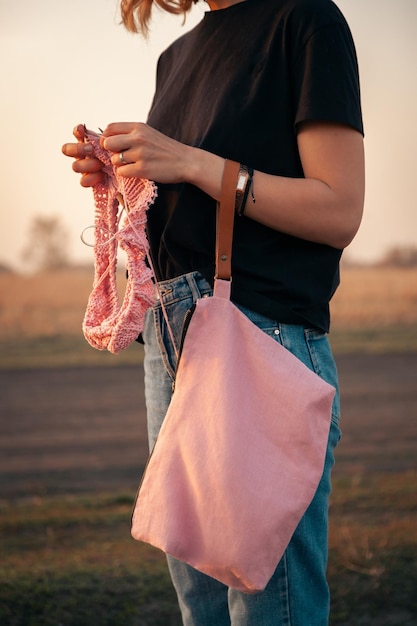 Outdoor atmospheric lifestyle photo of young beautiful darkhaired woman smiling and knitting with knitting crochet from a natural woolen thread a pink sweate