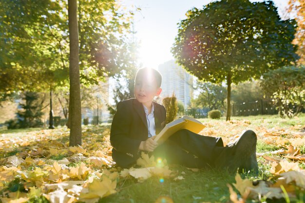 Outdoor autumn portrait of schoolboy reading book