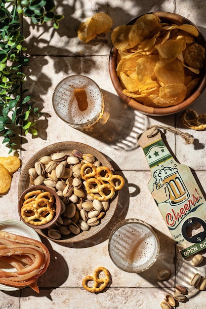 Outdoor beer party concept with beer in glasses snacks chips nuts pretzels on tile top view