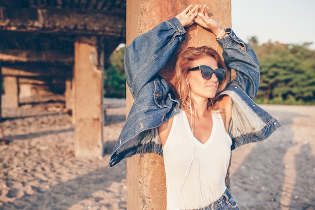 Photo outdoor fashion portrait of stylish girl wearing jeans jacket on the beach.