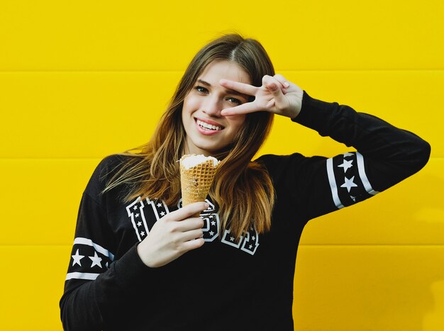 Outdoor fashion portrait of young hipster girl with  ice-cream on yellow wall background