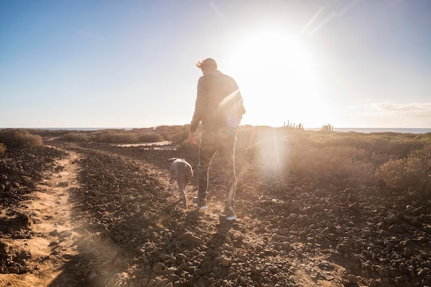 Outdoor leisure activity for young man and nice big dog walking together in the country side near the ocean friendship and relationship concept during a beautiful sunset