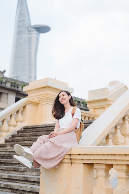 Outdoor lifestyle close up portrait of happy young woman in stylish casual outfit sitting on bridge on the street. Pretty hipster girl having fun and enjoying holidays.