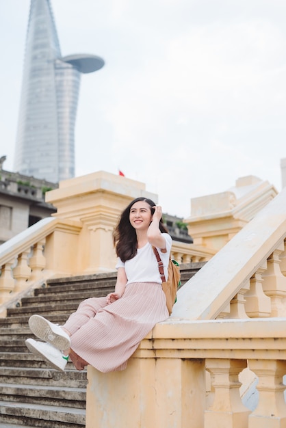 Outdoor lifestyle close up portrait of happy young woman in stylish casual outfit sitting on bridge on the street. Pretty hipster girl having fun and enjoying holidays.