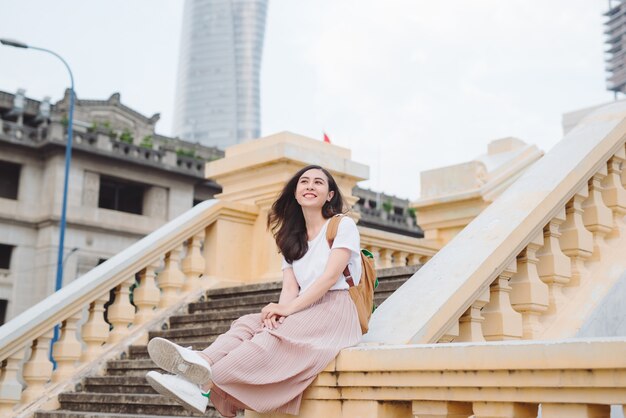 Outdoor lifestyle close up portrait of happy young woman in stylish casual outfit sitting on bridge on the street. Pretty hipster girl having fun and enjoying holidays.