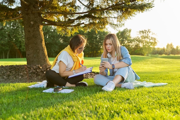 Outdoor meeting of teenage girl and woman of psychologist social worker, women talking sitting on green lawn in park, comfortable environment for talking with young people, mental help consultation