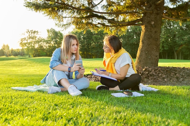 Outdoor meeting of teenage girl and woman of psychologist social worker, women talking sitting on green lawn in park, comfortable environment for talking with young people, mental help consultation