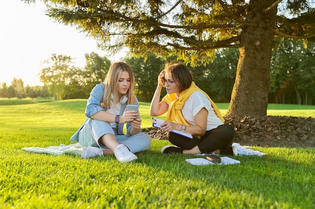 Outdoor meeting of teenage girl and woman of psychologist social worker, women talking sitting on green lawn in park, comfortable environment for talking with young people, mental help consultation