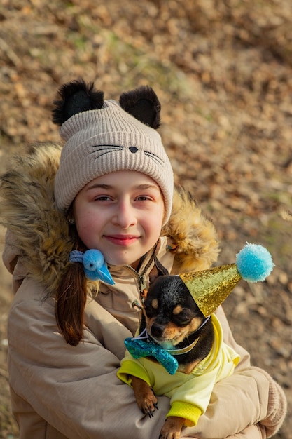 Outdoor portrait of 10- 11 year old girl wearing warm beige jacket with a chihuahua dog. birthday