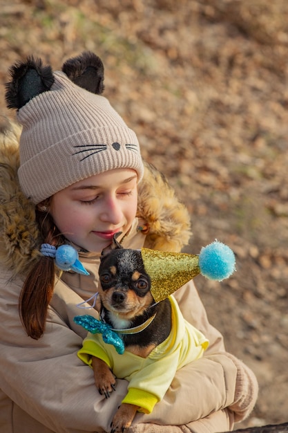 Outdoor portrait of 10- 11 year old girl wearing warm beige jacket with a chihuahua dog. birthday