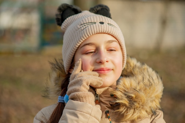 Outdoor portrait of adorable 10- 11 year old girl wearing warm jacket. A schoolgirl in a beige hat.