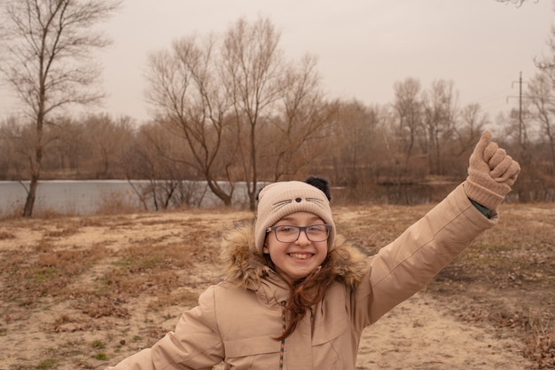 Outdoor portrait of adorable 10- 11 year old girl wearing warm jacket. A schoolgirl in a beige hat.