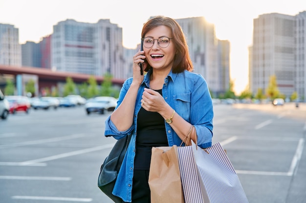 Outdoor portrait of a beautiful 40s woman talking on phone with shopping bags