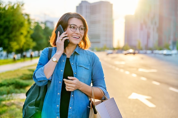 Outdoor portrait of a beautiful 40s woman talking on phone with shopping bags