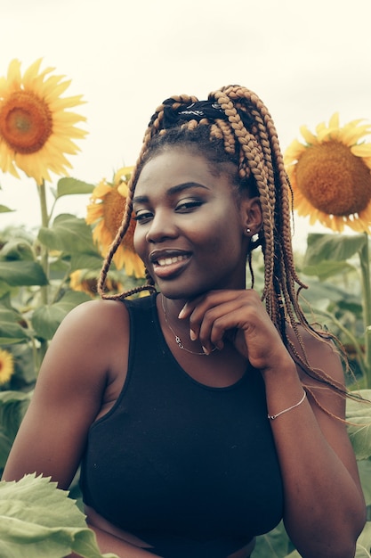 Outdoor portrait of beautiful happy mixed race African American girl teenager female young woman in a field of yellow flowers at sunset golden evening sunshine