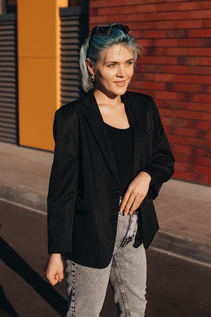 Outdoor portrait of bluehaired businesswoman walking down the streets wearing black jacket and sungl