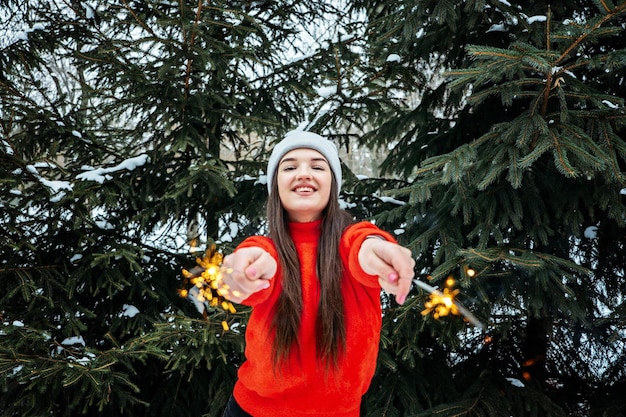 Outdoor portrait of happy cute latina girl in winter hat and red sweater posing with sparkler