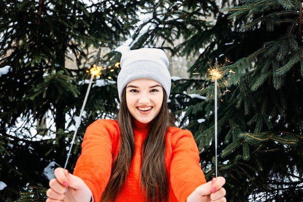 Outdoor portrait of happy cute latina girl in winter hat and red sweater posing with sparkler