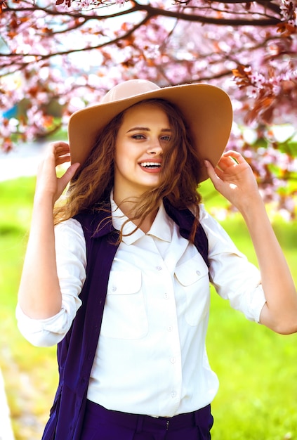 Outdoor portrait of young beautiful fashionable lady posing near flowering tree.