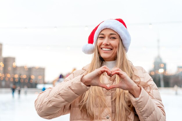 Outdoor portrait young beautiful fashionable woman wearing Santa hat posing street of European city Winter Christmas holidays concept