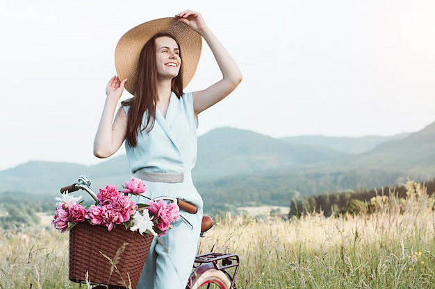 Outdoor portrait of young happy smiling woman in hat and enjoys mountain nature during the sunset. 