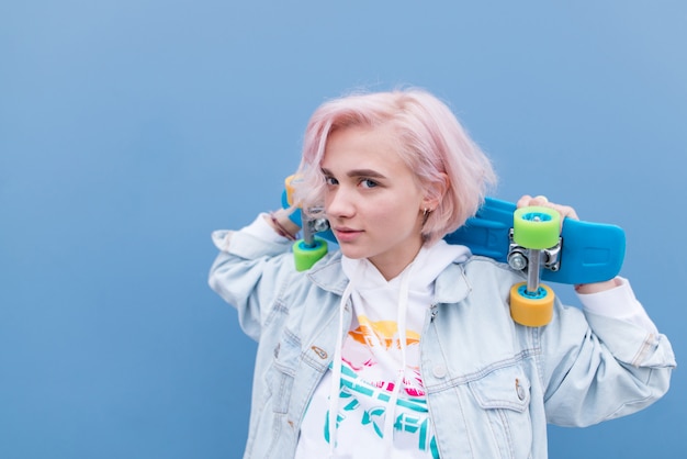 Outdoor portrait of a young pretty girl with skateboard on a blue wall